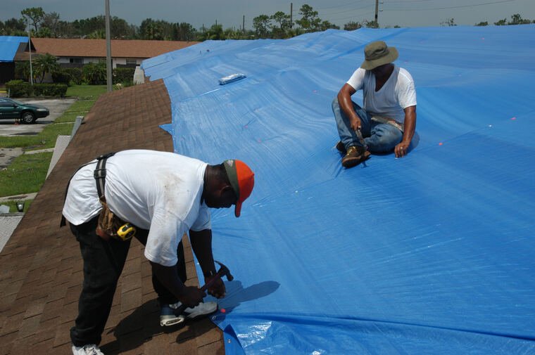 Workers covering a hurricane-damaged roof with a tarp